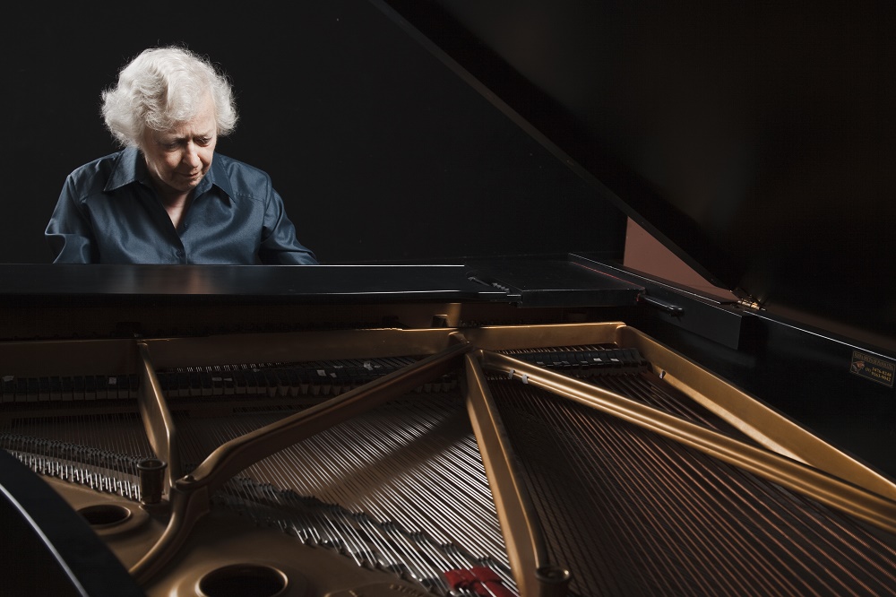 Mulher de cabelos grisalhos sentada atrás de um piano