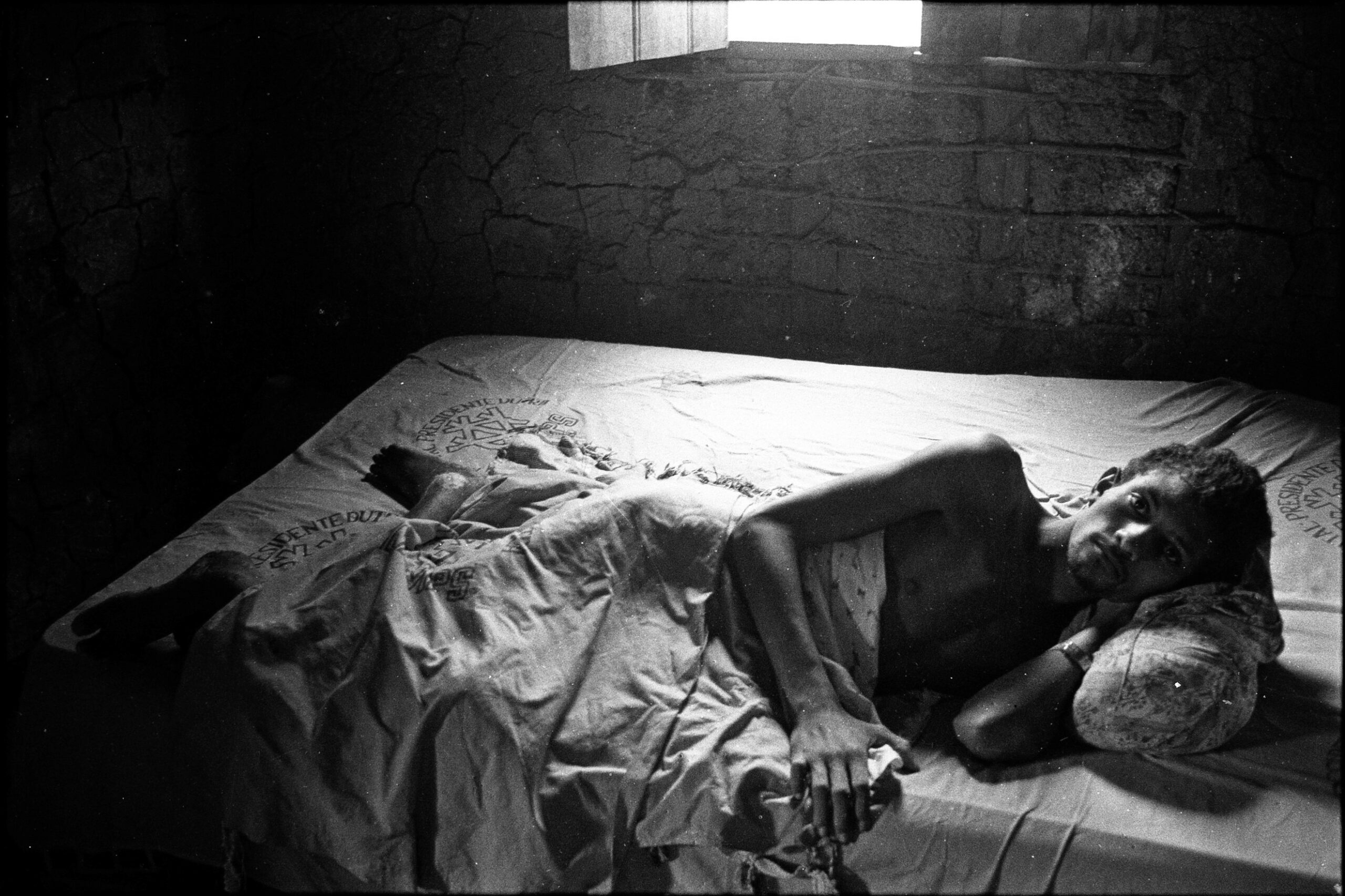 Um homem está deitado em uma cama, enrolado em um lençol.