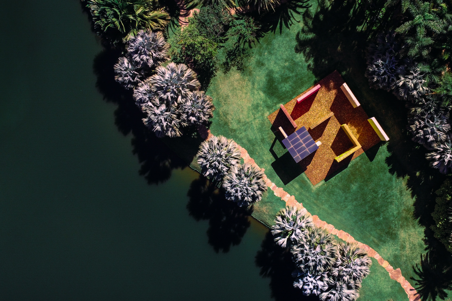 Vista aérea de área arborizada com lago ao lado e construções arquitetônicas coloridas.