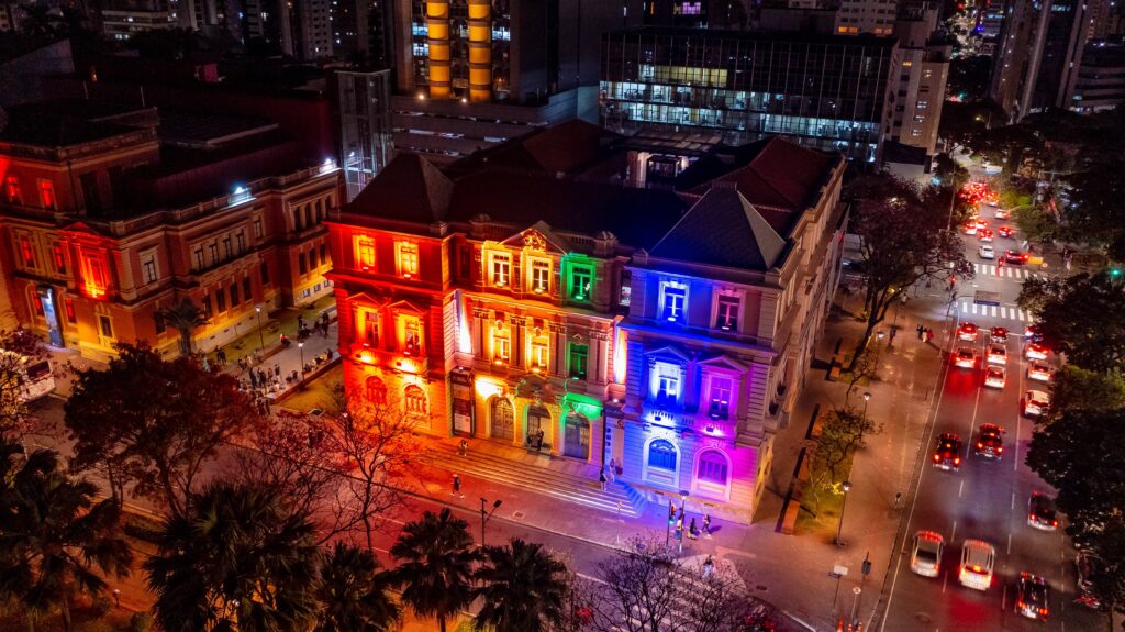 Imagem aérea do museu iluminado com as cores do arco-íris, que ilustram a bandeira do orgulho LGBTQIA+.