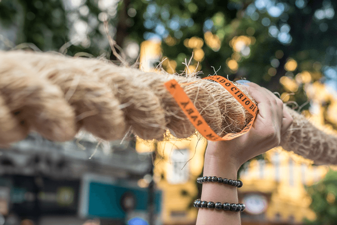 Imagem de uma mão segurando a corda do Círio. Na corda, há um fitinha laranja